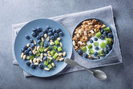 Healthy breakfast with granola cereal with blueberry, kiwi, yogurt and peanuts in blue bowl on a stone. Morning sweet dessert snack.  top viewの写真素材