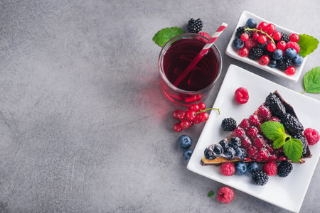 Sweet dessert cake with fresh blackberry, raspberry, currants and blueberry and green mint, red lemonade berry drink on stone table. copy space text. top viewの写真素材