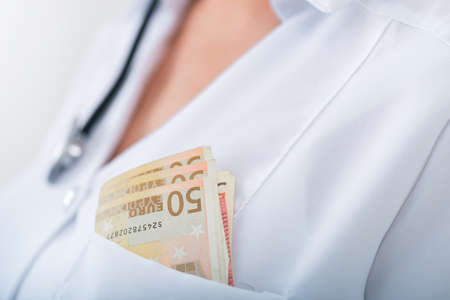 Doctor in clinic with a bundle of euro money. Corruption and bribe in medicine. Paid treatment.の写真素材