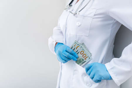 Doctor in clinic with a bundle of dollar bills. Corruption and bribery in medicine. Paid treatment. copy space for textの写真素材