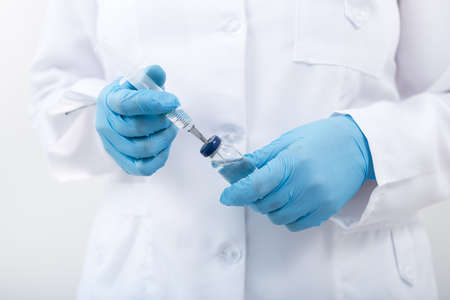 Woman doctor holding flu vaccine and syringe in hands on a white background. medical injection in hand and vaccination.の写真素材