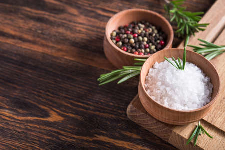 Closeup of spices salt and black papper, rosemary in bowl on a wooden tableの写真素材