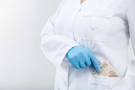 Doctor in clinic with a bundle of euro money. Corruption and bribe in medicine. Paid treatment. copy space for textの写真素材