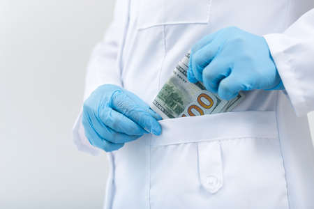 Doctor in clinic with a bundle of dollar bills. Corruption and bribery in medicine. Paid treatment.の写真素材