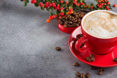 Cappuccino or latte with milk foam in a red cup with brazilian arabica coffee berries on a stone backgroundの写真素材
