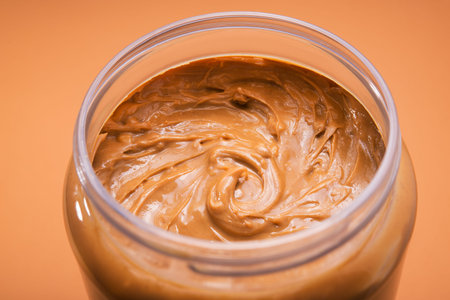 Closeup of open jar with peanut butter on a yellow background. traditional american breakfast.