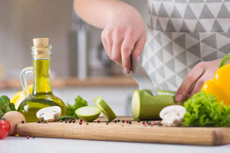 Close up of woman hands cutting vegetables in a kitchen table. Recipes for proper nutrition. Healthy Eating. Ingredients for vegetable pie.の写真素材