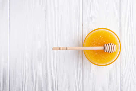 Sweet honey in a jar with dipper on a white wooden background. top viewの写真素材