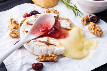 Tasty dessert with grill camembert cheese, grapes, nuts and cranberry jam on a dark wooden backgroundの写真素材