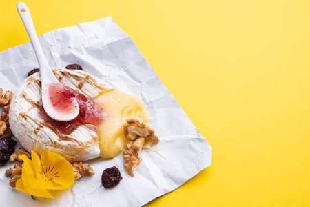 Grilled brie cheese with cranberry jam and nuts on a yellow backgroundの写真素材