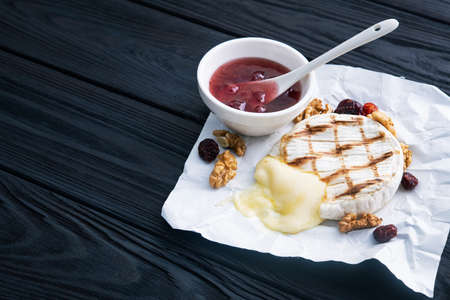 Tasty dessert with grill camembert cheese, grapes, nuts and cranberry jam on a dark wooden backgroundの写真素材