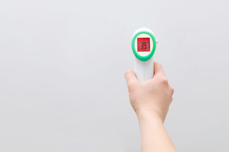 Female doctor holding electronic thermometer pointing at camera on a white background. Disease...