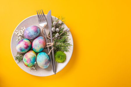 Easter table setting with colored eggs and willows branches on a yellow background. top view....