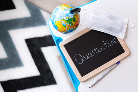 Wooden board school with quarantine text, globe and medical mask on a table.