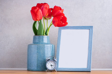 Beautiful red flowers tulips in a vase with clock and blank photo frame.の写真素材