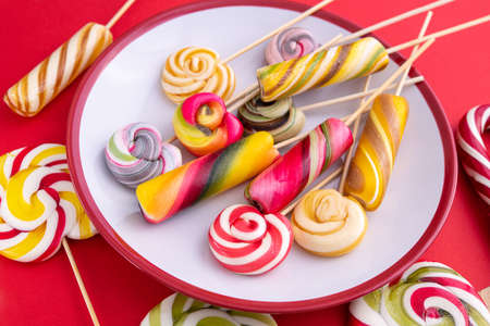 Colored sweet candy lollypops on a plate, red background. Favorite child food. Top view.の写真素材