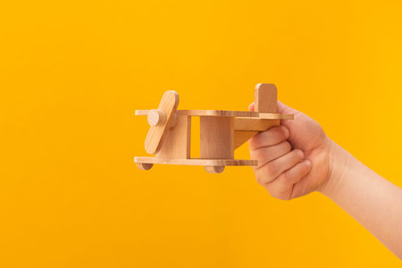 Baby hand holding retro wooden plane toy on a yellow backgroundの写真素材