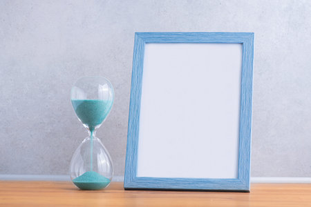 Blue wooden frame for photo with hourglass on a wall background. Concept of the transience of time. の写真素材