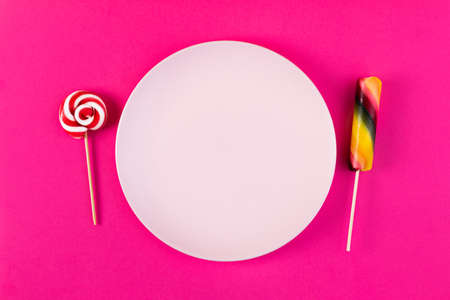 Concept of not working diet with sweet candy and empty plate on pink background. Flat lay. Top view. Food for real ladies.の写真素材