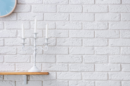 White candlestick on a wooden shelf. Scandinavian room style. White decorative brick on the wall.