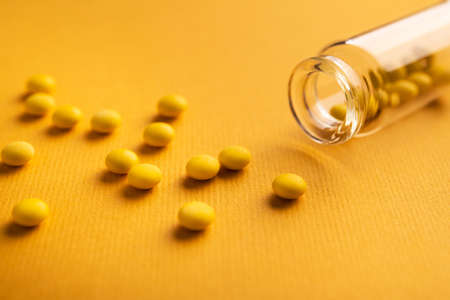 Closeup of small round pills with glass bottle on a yellow background.の写真素材