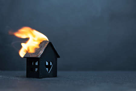 Black little wooden house caught fire on dark background. Concept of failure and compulsory home insurance.の販売画像