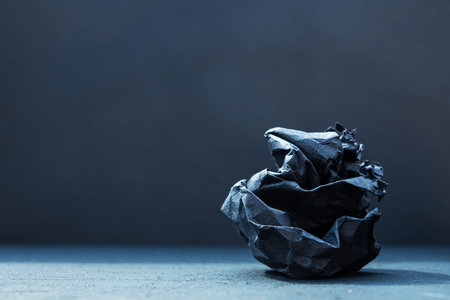Black crumpled paper ball on dark background. Concept of bad idea.
