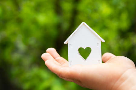 Small white model of house with heart window stand on child hand at green outdoors background.の写真素材