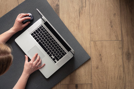 Left-handed girl working on a laptop lying on the floor. Online home training.