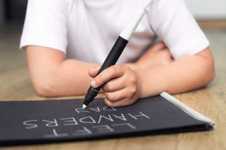 Left-handed child with a marker writes words on a notebook.の写真素材