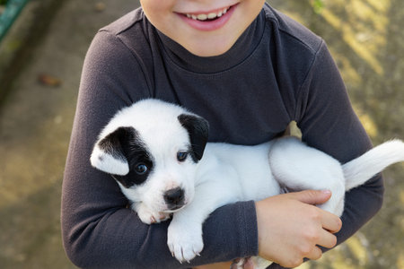 Child boy holding small black and white puppy dog walk near the house. animal love and care concept.