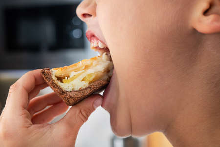 Closeup photo of boy mouth with fruit cake in kitchen. Improper nutrition concept.の写真素材