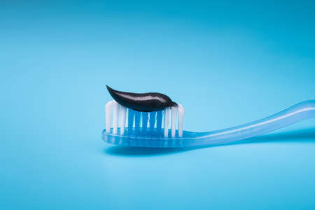 Black charcoal toothpaste on a toothbrush, blue background.の写真素材