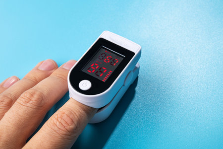 White new pulse oximeter on a blue table. measuring blood pressure and oxygen levels. pandemic examination Covid 19. the patient's hand.の写真素材