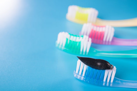 Set of four colorful toothbrushes with black charcoal paste on a blue background.