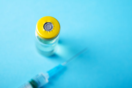 Bottle of coronavirus vaccine with syringe for injection. Vaccination against pandemics. Blue background.の写真素材