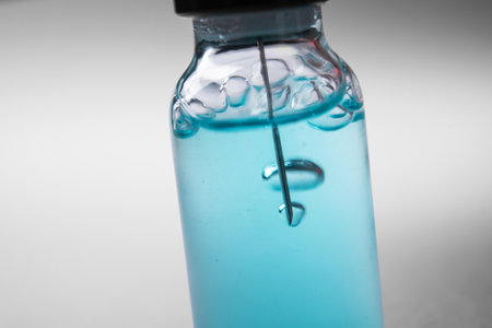 Closeup of glass bottle with coronavirus medication. Laboratory studies of the vaccine. White background table. Needle and air bubbles. Vaccine development.の写真素材