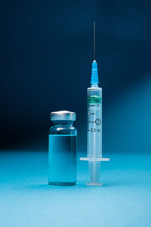 Bottle of coronavirus vaccine with syringe for injection. Vaccination against pandemics. Blue...