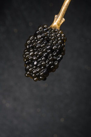 Closeup of golden vintage spoon filled with black caviar on dark background. rich, gourmet,...