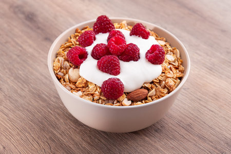 Sweet breakfast with granola, yogurt and fresh raspberries on a wooden table. Healthy food snack.
