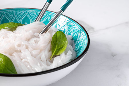 Boiled rice noodles in a bowl with fresh spinach leaves. The dish stands on a marble slab. east and...
