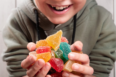 Child boy holding a big mountain of colorful sugar candy in his hands. Addiction to sweet foods.
