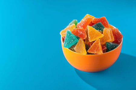 Colored sweet marmalade jelly candies in an orange plate on a blue background.