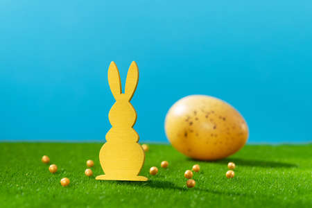 Easter holiday. Wooden rabbit decor. Colored spring eggs on green grass. blue background.の写真素材