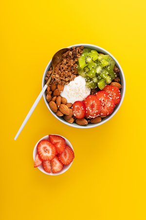 Granola with yogurt, kiwi, almond nuts, strawberry in a bowl. Minimal concept food. Healthy eating. yellow background. top view.の写真素材