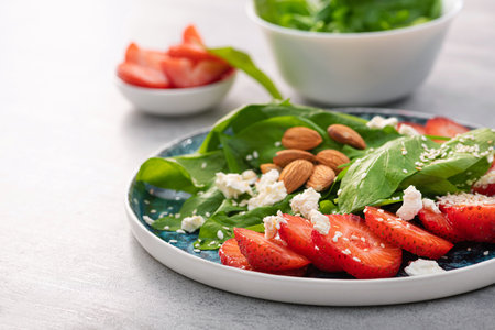 Fresh salad with strawberry fruit, almond, spinach and cottage cheese on a plate. concrete background. Diet and vegan food.の写真素材