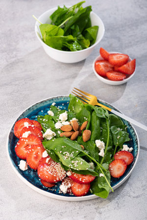 Fresh salad with strawberry fruit, almond, spinach and cottage cheese on a plate. concrete background. Diet and vegan food.の写真素材