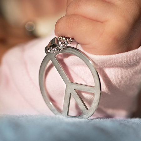 Hand of infant holding metal necklace peace symbol. War in Ukraine. Stop the occupation and aggression.の写真素材