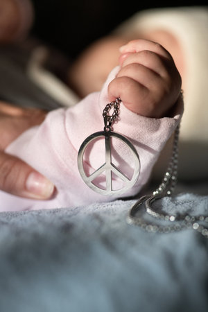 Hand of infant holding metal necklace peace symbol. War in Ukraine. Stop the occupation and aggression.の写真素材