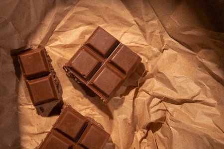 Chocolate bar pieces on kraft paper. Warm light concept background. Tp view.の写真素材